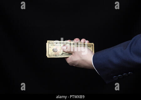 Die Hand eines Mannes im Anzug hält Dollar auf schwarzem Hintergrund Stockfoto