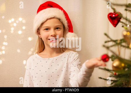 Happy girl in santa hut schmücken Weihnachtsbaum Stockfoto