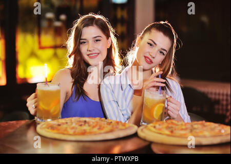 Zwei junge hübsche Mädchen essen Pizza und Bier trinken ein Bier oder Cocktail in der Bar oder in der Pizzeria Stockfoto