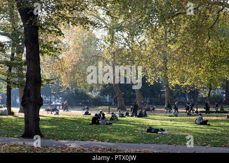 Russell Square im Herbst Sonnenschein mit Menschen sitzen auf Gras im dunstigen Sonnenschein und Blätter auf dem Boden Bloomsbury Camden London England Großbritannien UK Stockfoto