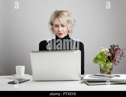 Junge attraktive Frau, die an einem Notebook arbeitet vor grauem Hintergrund. Stockfoto