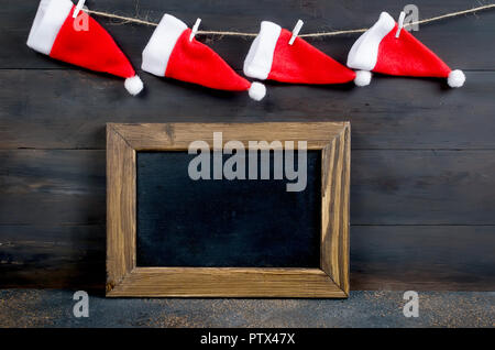 Santa's Hüte hängen an der Wand und ein leeres Schwarzes Brett für Text, Weihnachtskarte mit leeren Platz für Text, kopieren Raum Stockfoto