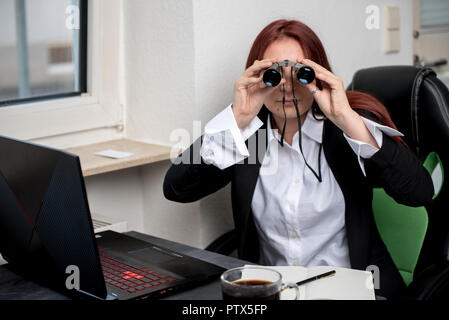 Eine junge Frau im Büro ist auf der Suche durchs Fernglas direkt im Viewer Stockfoto