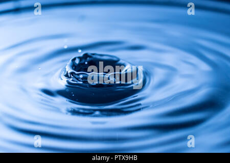 Wassertropfen spritzen in einem Glas blau Stockfoto