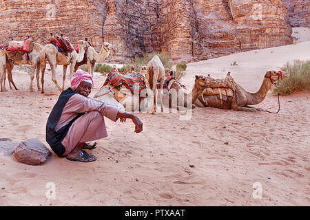 WADI RUM, Jordanien - Juni 14, 2016: ein beduine Kamel herder liegt in der Nähe von seiner Herde Kamele in einem Der siqs des Wadi Rum Wüste in Jordanien. Stockfoto