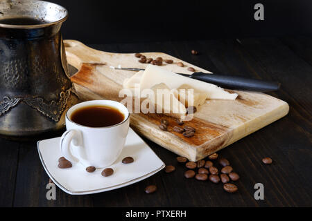 Kleine Tasse schwarzen Kaffee, türkischer Kaffee Topf und Käse auf dem Schneidbrett auf dunklem Hintergrund Stockfoto
