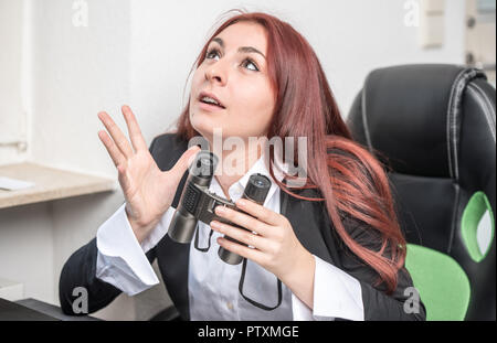 Young Business Frau im Büro, am Schreibtisch vor einem Laptop, mit Fernglas in der Hand, sagt sie etwas, erklärt Stockfoto