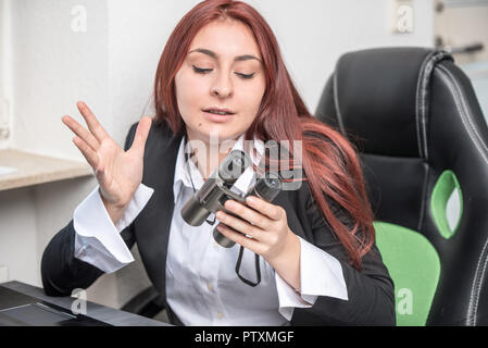 Young Business Frau im Büro, am Schreibtisch vor einem Laptop, mit Fernglas in der Hand, sagt sie etwas, erklärt Stockfoto