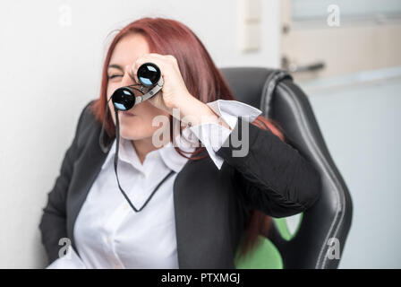 Eine junge Frau im Büro ist auf der Suche durchs Fernglas direkt im Viewer Stockfoto