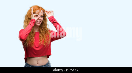 Junge rothaarige Frau mit Brille mit glücklichen Gesicht lächelnd tun ok Zeichen mit der Hand auf Auge schauen durch die Finger Stockfoto