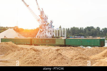 Port Lastkran Ladungen Holzhackschnitzel in Eisenbahnwaggons, Späne - Holz Stockfoto