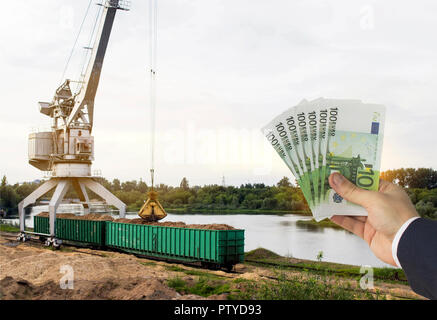 Eine Hand mit Euro Geld gegen ein hafenkran macht das Laden der Späne in Güterwagen, Euro exportieren Stockfoto