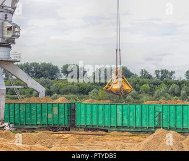 Port Lastkran Ladungen Holzhackschnitzel in Eisenbahnwaggons, Späne - Holz Stockfoto