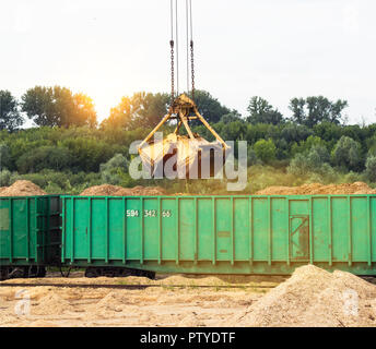 Der Hafenkran macht das Laden der Späne in die Güterwagen der Bahn, - aus der Nähe, Schöpfkelle, Greifer Stockfoto