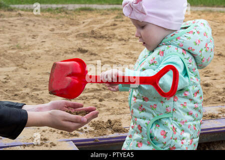 Ein kleines Mädchen spielt in der Sandbox mit ihrer Mama, in der Nähe Stockfoto