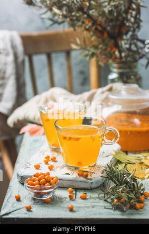 Vitaminic gesunden Sanddorn Tee in einem Glas Tassen mit frischen, rohen Sanddornbeeren auf einem weißen Holzmöbeln rustikal Hintergrund Stockfoto