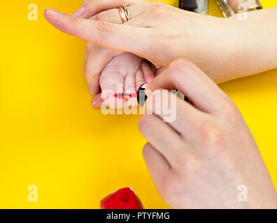 Eine Mutter malt Ihre Zehennägel mit ihrer kleinen Tochter, einen gelben Hintergrund, Nahaufnahme Stockfoto