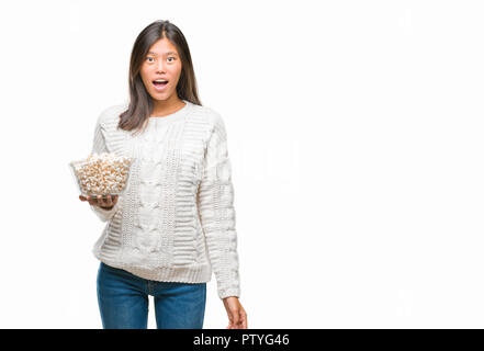 Junge asiatische Frau essen Popcorn über isolierte Hintergrund im Schlag mit einer Überraschung konfrontiert, ängstlich und aufgeregt mit Angst Angst Ausdruck Stockfoto