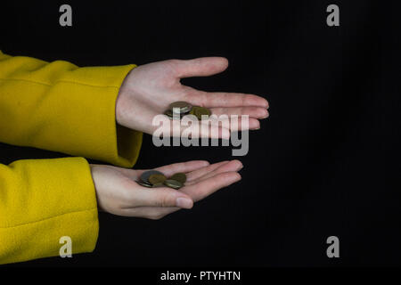 Mädchen mit ausgestreckten Händen, in denen Münzen, schwarzer Hintergrund, close-up Stockfoto