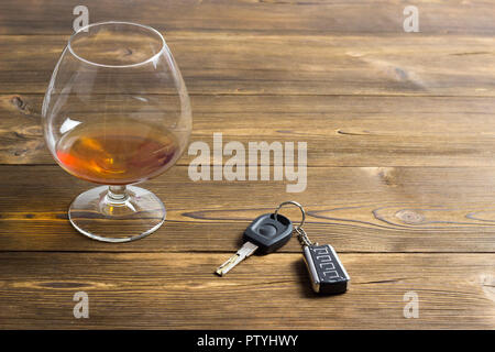 Autoschlüssel und ein Glas mit Alkohol auf einem hölzernen Hintergrund Stockfoto