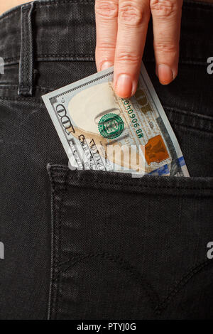 Weibliche Hand zieht eine 100 US-Dollar Bill aus ihrem schwarzen Jeans Tasche. Konzept der finanziellen Beziehungen Stockfoto