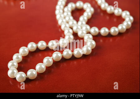 Weiße Perlenkette auf rötlich braunen Hintergrund. Selektiver Fokus und flache Tiefenschärfe. Stockfoto