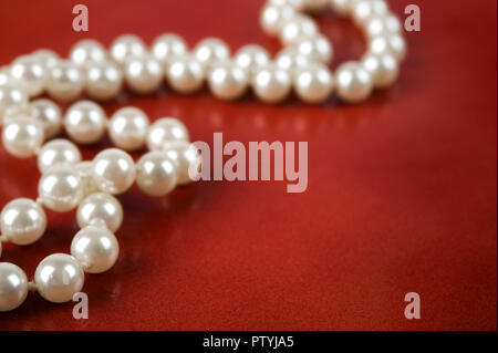 Weiße Perlenkette auf rötlich braunen Hintergrund. Selektiver Fokus und flache Tiefenschärfe. Stockfoto