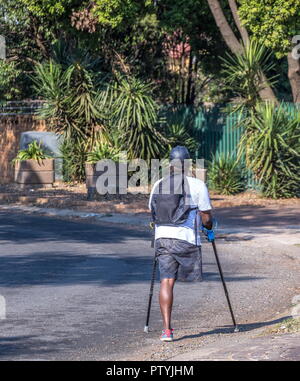 Johannesburg, Südafrika - Unbekannter körperlich Behinderte schwarzer Mann Kämpfe auf seine Krücken durch die Straße von einem Vorort Stockfoto