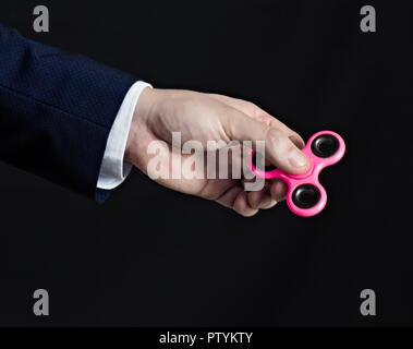 Ein Mann im Anzug hält einen Spinner in der Hand, einen schwarzen Hintergrund, ein Vorhang, der Plan Stockfoto