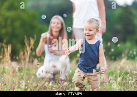 Glückliches Kind mit der Familie eine schöne Zeit bläst Seifenblasen im Freien Stockfoto