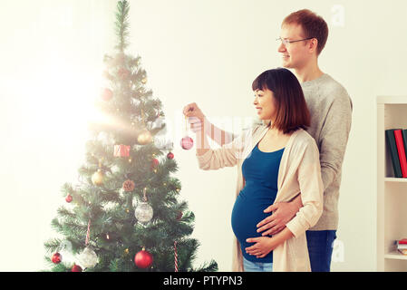 Gerne schwangere Ehefrau und Ehemann an Weihnachtsbaum Stockfoto