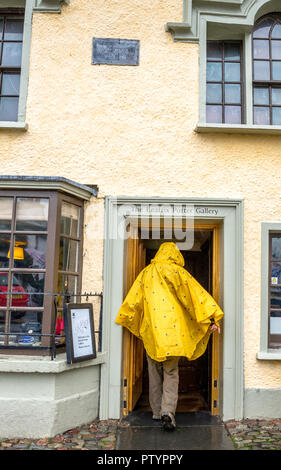 Weibliche touristische Eingabe der Beatrix Potter Gallery in Edinburgh, Cumbria an einem regnerischen Tag trägt einen Poncho. Stockfoto