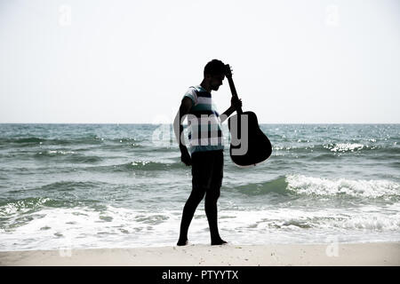 Junger Mann mit akustischer Gitarre am Strand, traurigen Emotionen Stockfoto