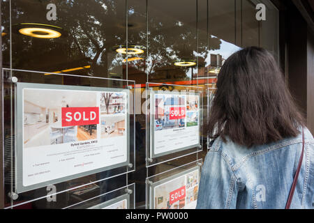 Eine junge Frau, die in ein Immobilienmakler-Fenster schaut und versucht, auf die Immobilienleiter zu gelangen, Barnes, London, Großbritannien Stockfoto