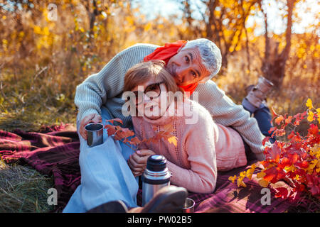 Senior paar Tee im Herbst Wald. Glücklich, Mann und Frau, genießen, Picknick und Natur. Lächelnd Mann gießt Kaffee aus der Thermoskanne Stockfoto