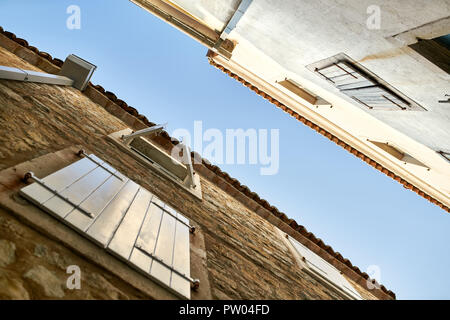 Fassaden der alten Häuser aus Stein mit Fenstern mit Fensterläden auf dem Hintergrund des blauen Himmels in Budva in Montenegro. Sonne scheint auf Sie. Horizontale. Stockfoto