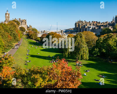 Menschen in die Princes Street Gardens sitzen im Herbst Sonne mit Balmoral Hotel Clock Tower und North Bridge, Edinburgh, Schottland, Großbritannien Stockfoto