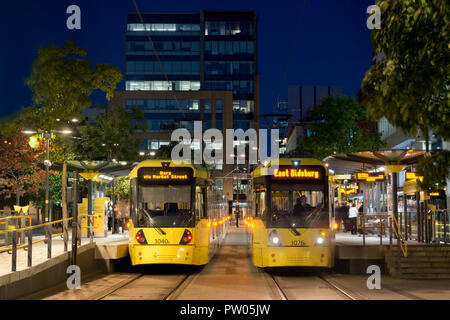 Zwei Metrolink Tram kommen am St. Peter's Square Stop in der Nacht im Stadtzentrum von Manchester, UK. Stockfoto