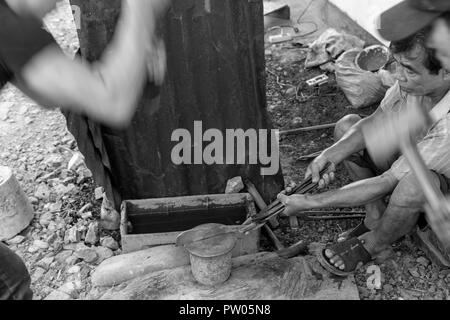 LUANG PRABANG, LAOS - OKTOBER 8: Ein unbekannter Mann hält ein Messer mit Zangen, während andere es in einem lokalen Dorf Hammer in Luang Prabang, Laos o Forge Stockfoto