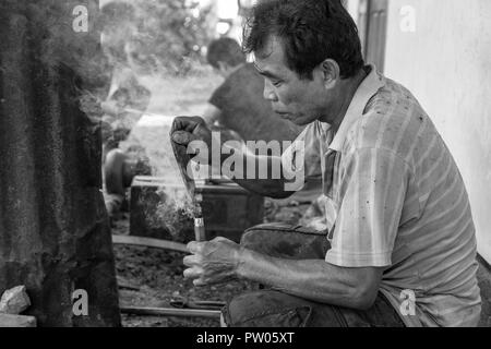 LUANG PRABANG, LAOS - OKTOBER 8: Ein unbekannter Mann brennt ein heißes Messer Tang in einem Griff in einem lokalen Dorf in Luang Prabang, Laos am 8. Oktober Forge Stockfoto