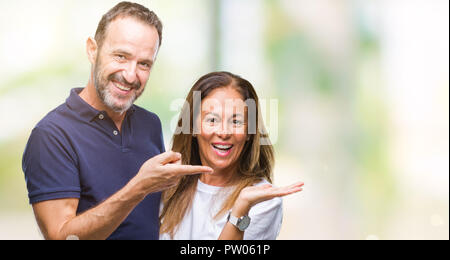Mittleres Alter spanischer casual Paar über isolierte Hintergrund erstaunt und lächelt in die Kamera während der Präsentation mit Hand und zeigte mit dem Finger. Stockfoto