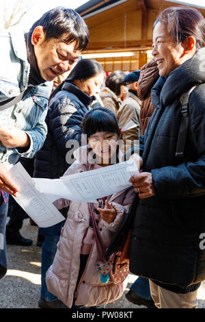 Japanische neues Jahr, shogatsu. Eltern, Bücken fortune Slip aus Omikuji Papier zu ihrer Tochter, Mädchen, 4-5 Jahre alt. Nishinomiya Schrein. Stockfoto