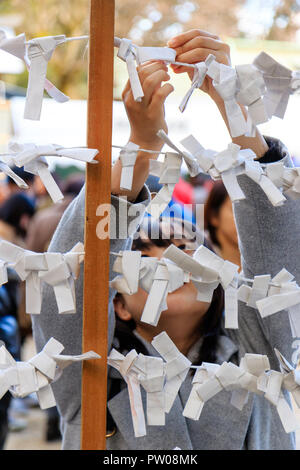 Japanische neues Jahr, shogatsu. Junge Frau bis schlechtes Vermögen Papierstreifen zu binden, Omikuji zu rahmen Pech hinter sich zu lassen. Nishinomiya Schrein. Stockfoto