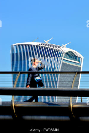 Mann (unscharf), die über die Millennium Bridge mit dem Walkie Talkie Gebäude (20 Fenchurch Street) im Fokus hinter, London, England, UK.