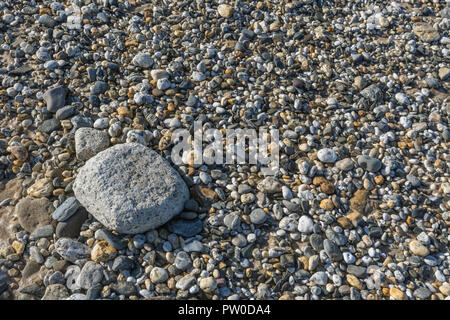 Größeres Gestein (möglicherweise aus Beton) allein auf Schindelbett aus kleineren Steinen und Kieselsteinen. Für 'Last man Standing', lassen Sie keinen Stein unverdreht Stockfoto