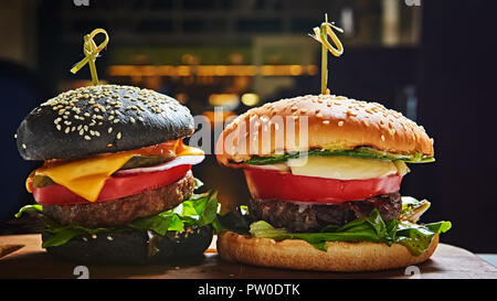 Satz von hausgemachten Burger in schwarze und weiße Brötchen mit Tomaten, Salat, Käse, Zwiebel auf Holz, das Board über Dark Tabelle. Im rustikalen Stil. Hausgemachte schnell Stockfoto