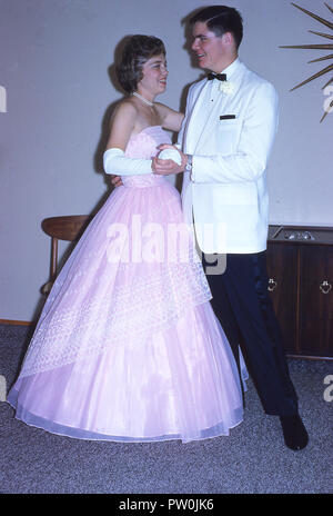 1962, Amerika, gehen zum Abschlußball ..... ein junger Mann mit einem weißen Smoking und und eine junge Frau eine lange Rüschen rosa Kleid stehen zusammen tragen für ein Bild, bevor Sie das Prom teilnehmen, ein traditioneller und wichtiger Ende der Amtszeit Tanz und gesellschaftliches Ereignis für uns Schülerinnen und Schüler. In den 50s und 60s, das Prom war mehr der Veranstaltung ein Paar, wo ein Junge ein Mädchen sein Date zu sein Bitten und würde Ihr Escort nach ihrer Abholung an ihrem Haus und viele Bilder gemacht! Stockfoto