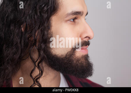 Closeup Profil Seitenansicht des stattlichen zuversichtlich Mann mit schwarzen Langen lockigen Haar und Bart, weg schauen mit Smile. Männliche Gesundheit und Schönheit Konzept. Stockfoto