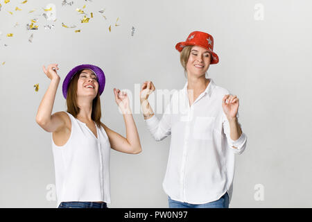 Gerne tanzen Junge weibliche Freunde lächelnd mit Konfetti gegen den weißen Hintergrund. Feiern Stockfoto