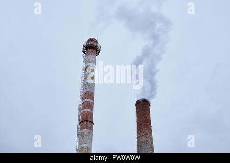 Rauchende Schlote vor dem Hintergrund des bedeckten Himmels. Industrielle Hintergrund. Stockfoto